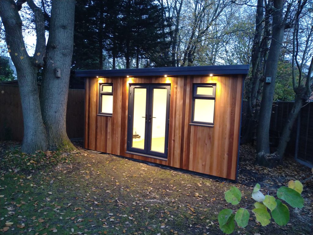 The Firwood Garden Room In St Albans - Exterior (Of A Small Garden Office Glowing With Lights At Night)
