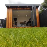 A wooden door and window adorn a garden office, set amidst lush plants