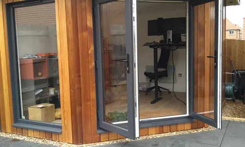 The Mallard Garden Room, St Albans - A Small Office Equipped With A Sliding Door, A Well-Organized Desk With A Computer, Chair, Storage Shelves, And Office Supplies