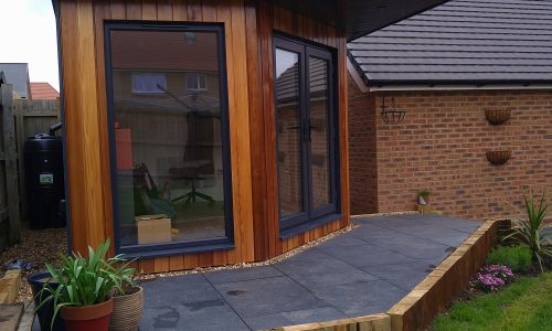 The Mallard Garden Room In St Albans - Finished Garden Room With Wooden Cladding, Large Windows, And A Landscaped Patio Area