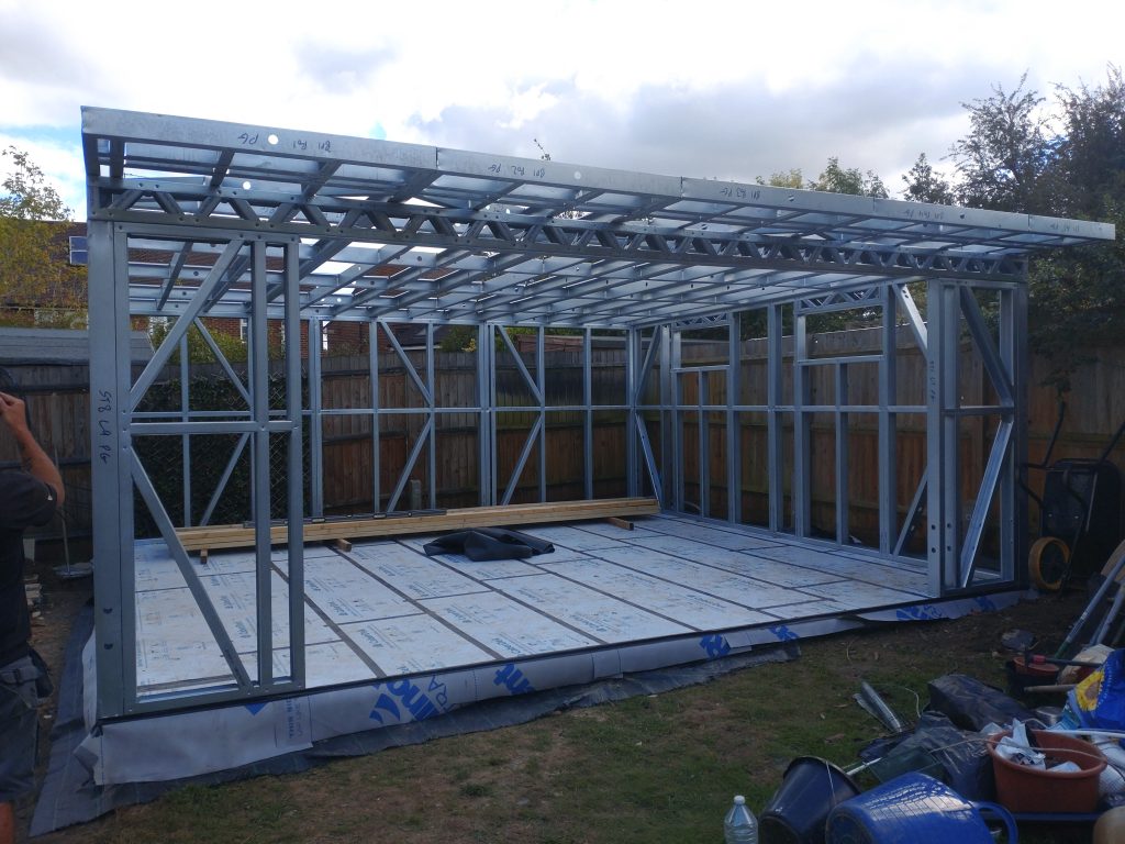 A metal structure under construction in a backyard, with tools and materials scattered around the site
